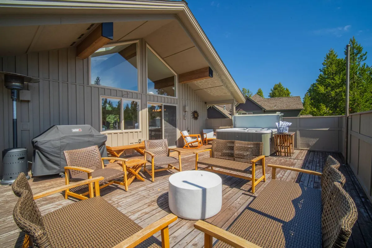 This exterior image showcases a spacious outdoor deck featuring a hot tub, comfortable seating area, and grill surrounded by tall trees. The atmosphere is relaxed and inviting, perfect for unwinding after a day on the golf course. Sunset lighting and the presence of the hot tub create a sense of leisure and comfort.