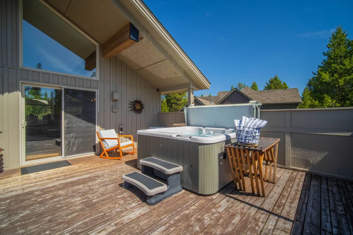 A spacious wooden deck with a bubbling hot tub and lounge chair, accented by outdoor decor. The deck is designed for relaxation, whether sunbathing, stargazing, or unwinding after a day of adventure in the nearby mountains or river.