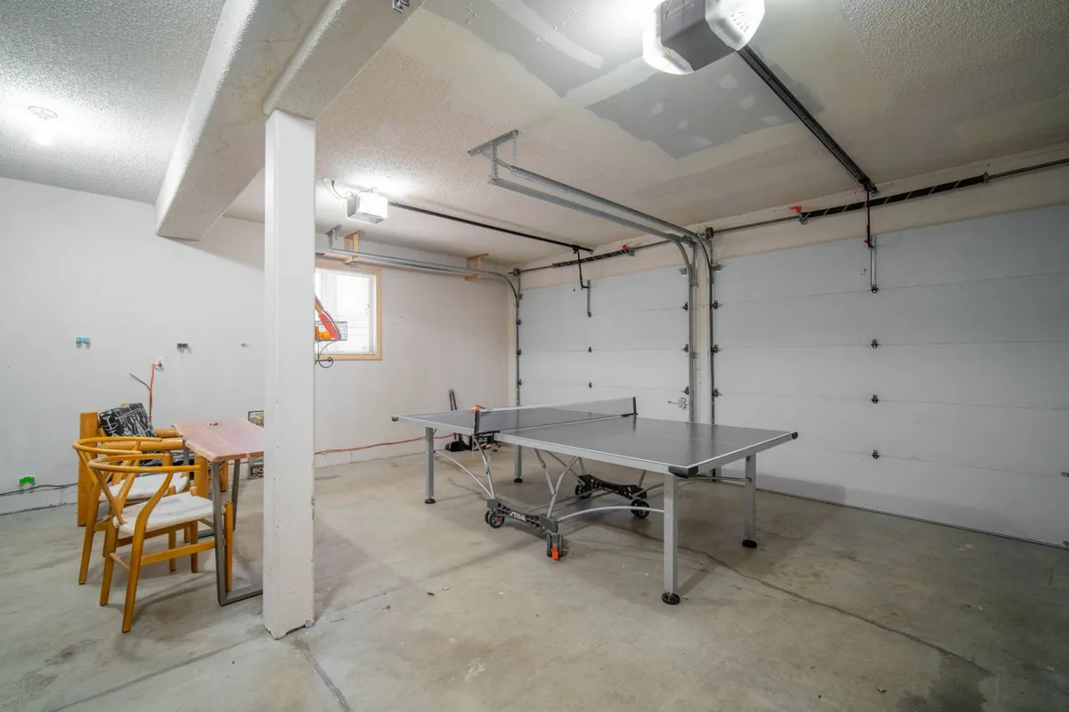 A ping pong table set up in front of a garage door with wooden chairs and a small table nearby. The laid-back arrangement invites both play and spectating, capturing the spirit of group fun and easy transitions between lounging and gaming.
