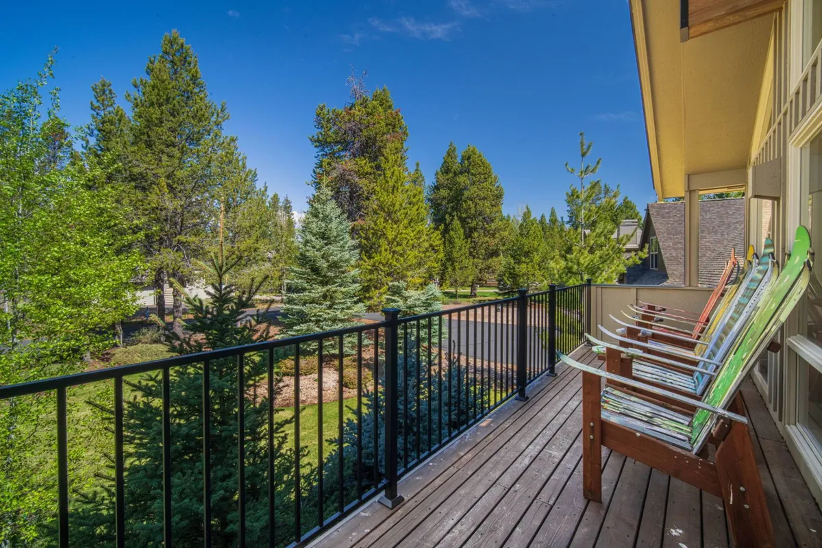 A serene exterior balcony with comfortable seating overlooks lush greenery and a vast blue sky, creating a perfect spot to relax and take in the natural surroundings. The inviting balcony seamlessly connects the home to the outdoors, emphasizing the beauty of the Sunriver landscape.