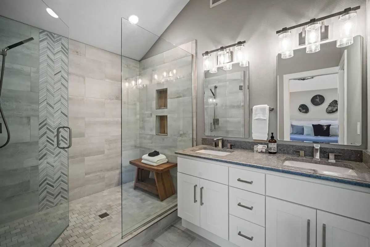 A spa-inspired bathroom featuring a glass shower with modern fixtures, a double sink vanity, and contemporary wall art. The clean lines and serene color palette evoke a luxurious, refreshing experience.