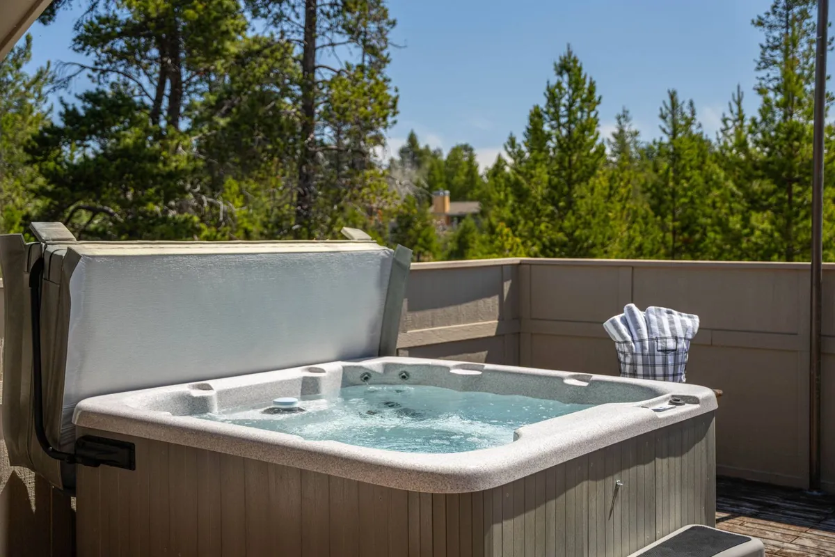 An inviting outdoor scene featuring a hot tub nestled amongst pine trees, with a towel draped beside it. The mood is tranquil and serene, suggesting relaxation and connection with nature after an active day.
