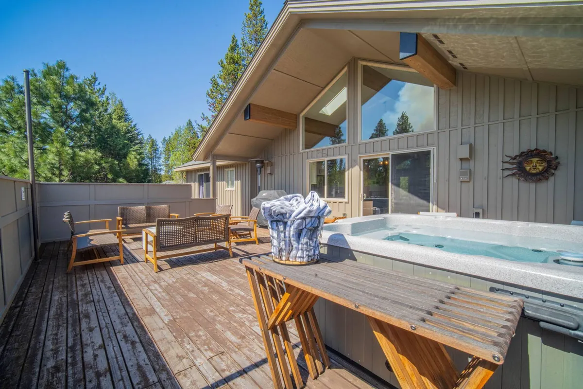 A cozy hot tub sits on a wooden deck encircled by tall trees, with plush seating nearby. The scene feels intimate and tranquil, perfect for stargazing or relaxing after a day outdoors. The natural setting and outdoor furnishings create a retreat-like ambiance ideal for unwinding and connecting with nature.